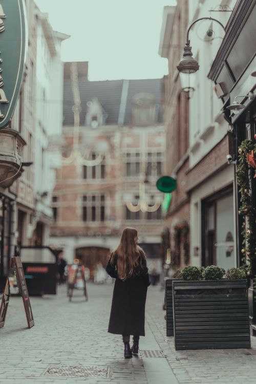 Free Stylish woman walking in a cozy, decorated urban street, perfect for travel and fashion themes. Stock Photo