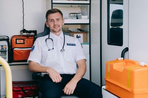 Free A cheerful paramedic sits inside an ambulance, ready for action in his medical uniform. Stock Photo