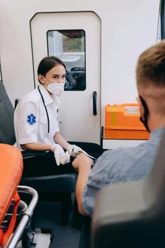 A paramedic wearing a mask assists a patient inside an ambulance, ensuring safety and care.