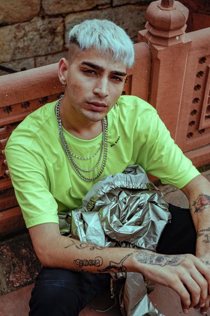 Fashionable man with vibrant style and tattoos poses confidently outdoors.