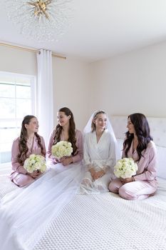 Bride and bridesmaids sharing a joyful moment in matching pink pajamas before the wedding ceremony.
