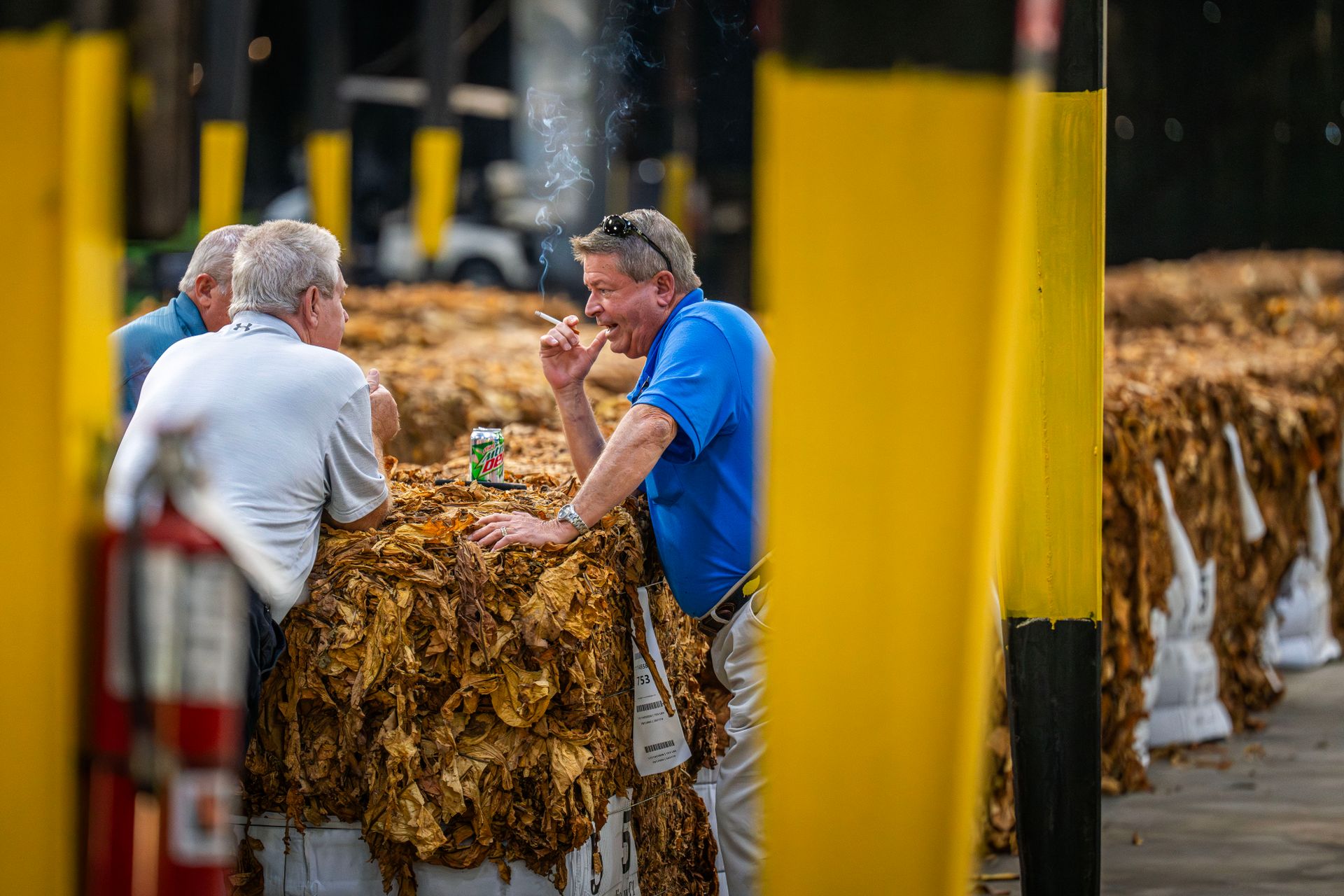 Group of men engaging over tobacco bundles in an outdoor market setting.