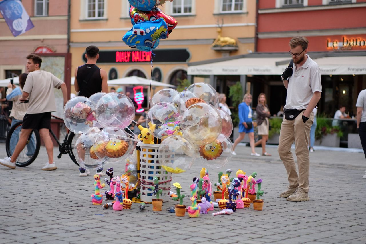 a lively street market with balloons toys and people enjoying a festiv