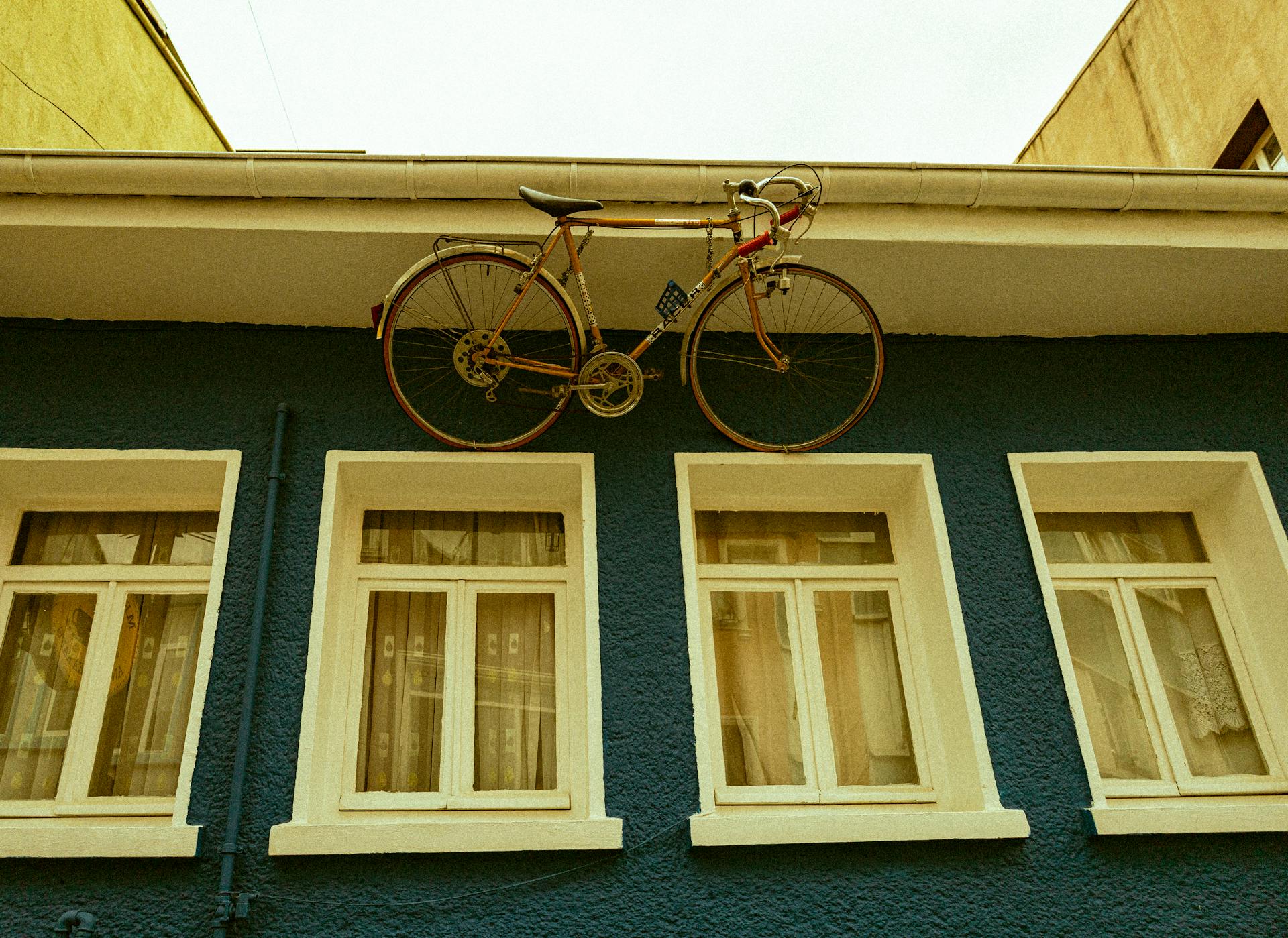 Quirky bicycle mounted above windows on a blue building facade in Bursa, Türkiye.