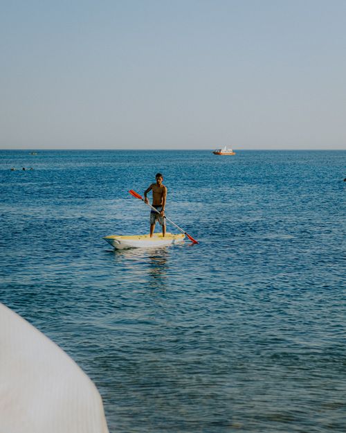 Free A man stands on a paddleboard with an oar on a calm sea under blue skies Stock Photo