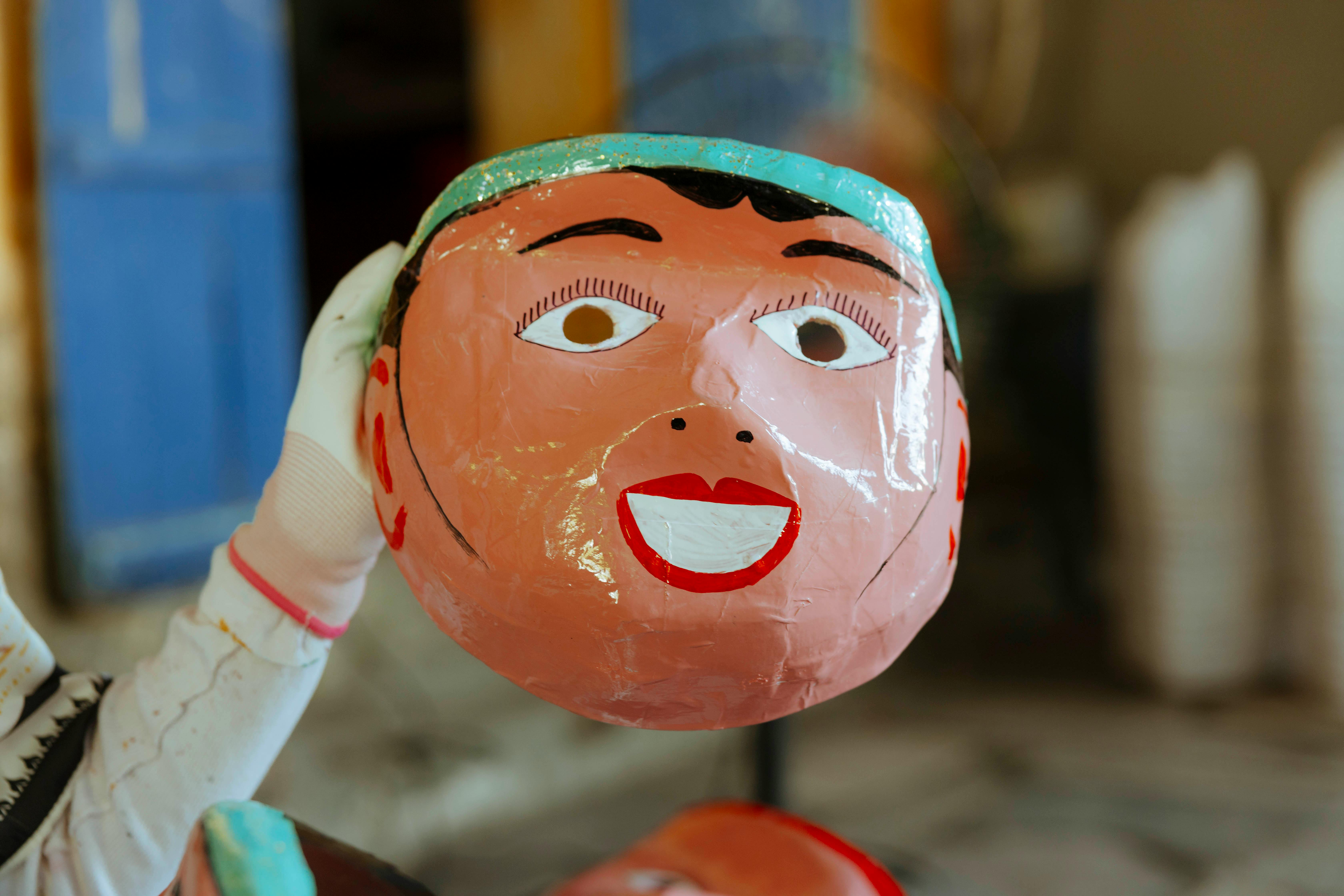 Colorful papier-mâché head sculpture held indoors, showcasing handmade craftsmanship and traditional art.