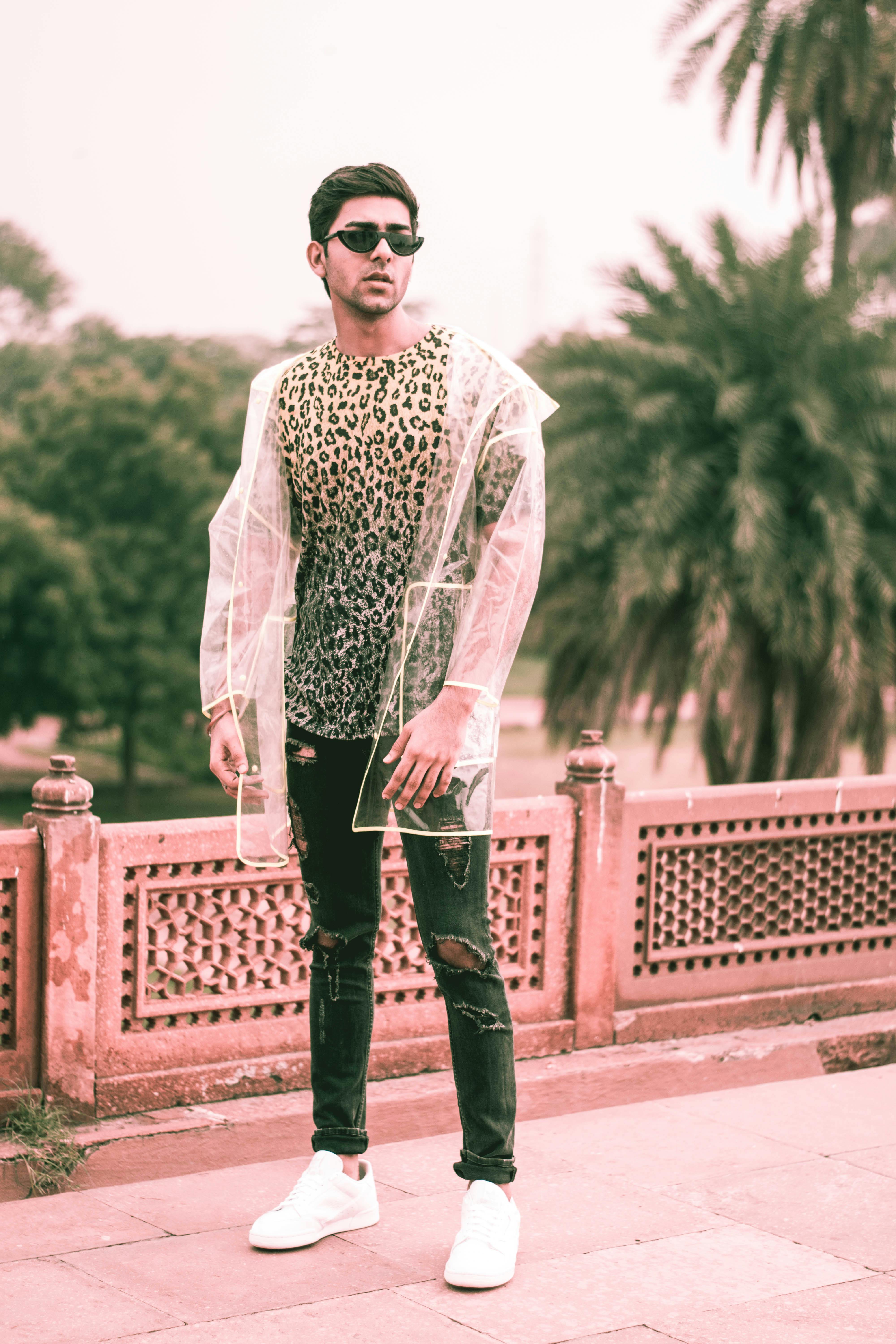 一位时尚男子在户外穿着透明雨衣，内搭豹纹衬衫摆姿势，散发着时尚气息