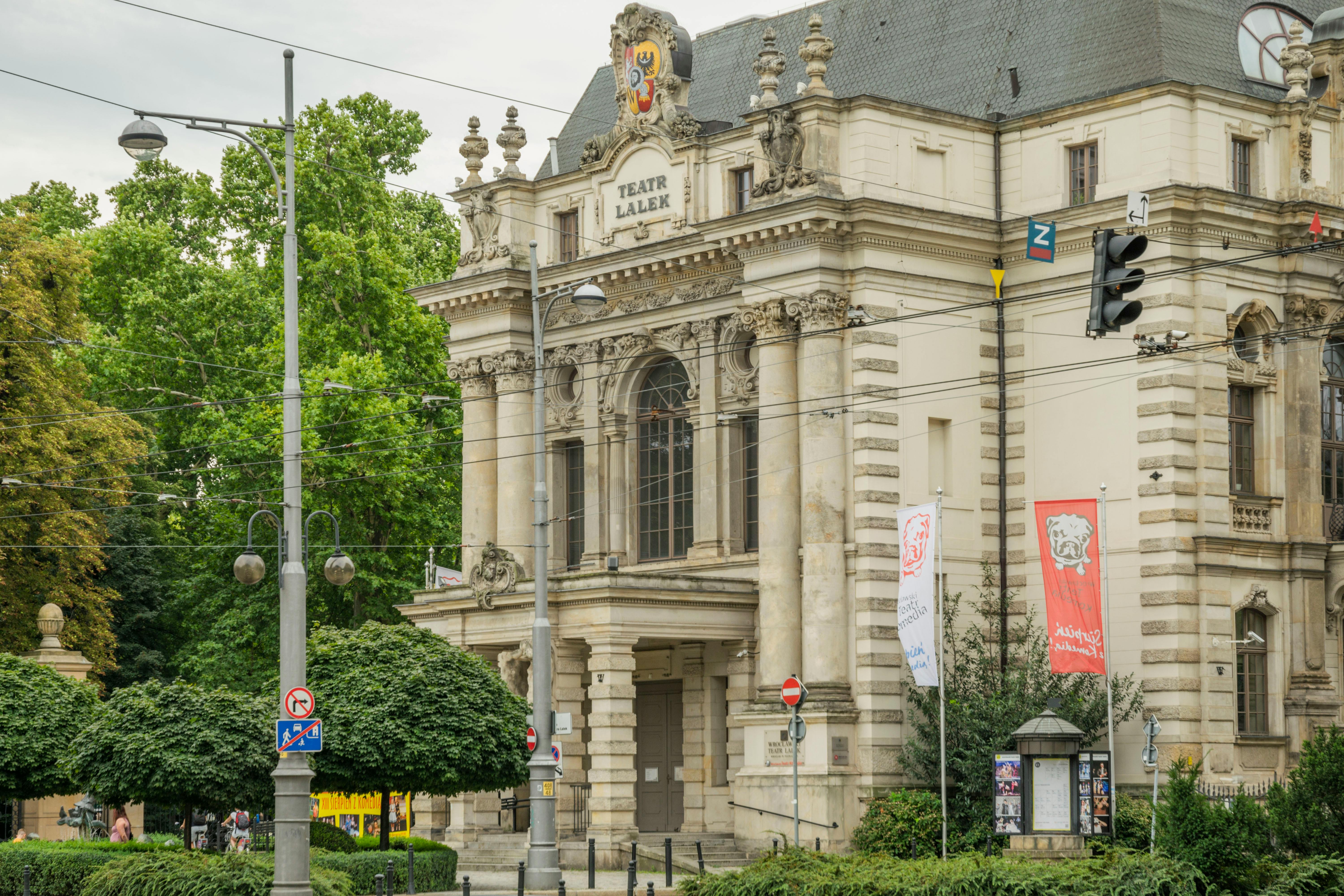 Free Historic Wrocław Puppet Theater facade amidst city life and greenery. Stock Photo