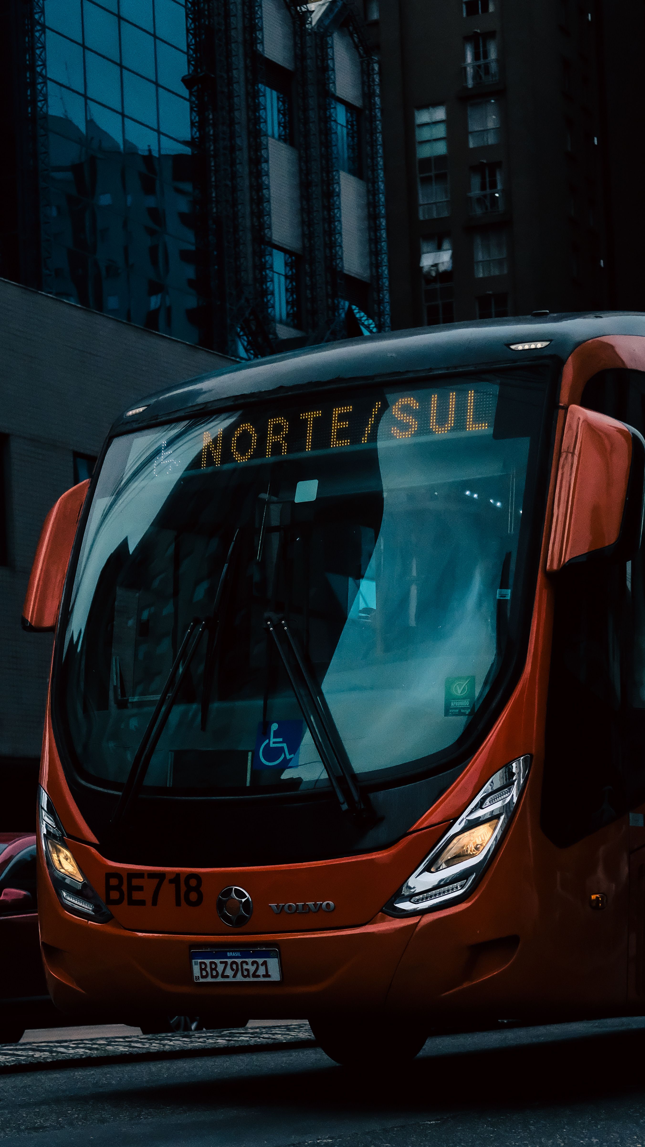 Red city bus labeled 'NORTE/SUL' in downtown urban setting with tall buildings.