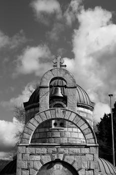 Black and white photo of a historic church dome with a cross and cloudy sky.