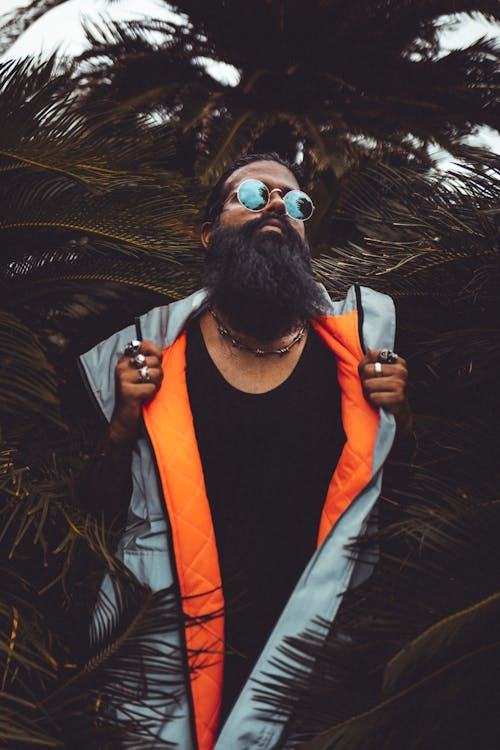 Man Wearing Grey and Orange Zip-up Vest Beside Palm Plant