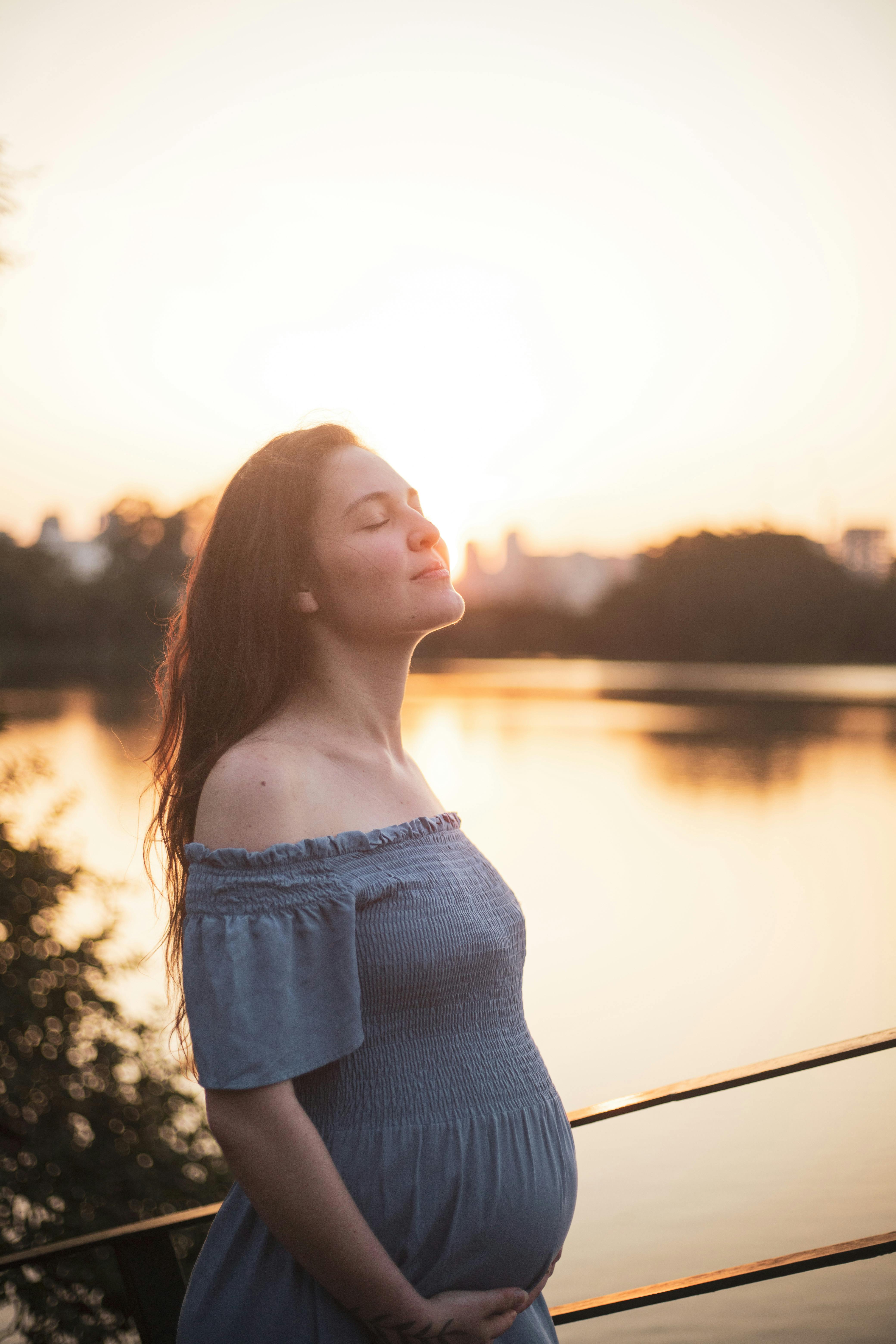 a pregnant woman standing by the water at sunset