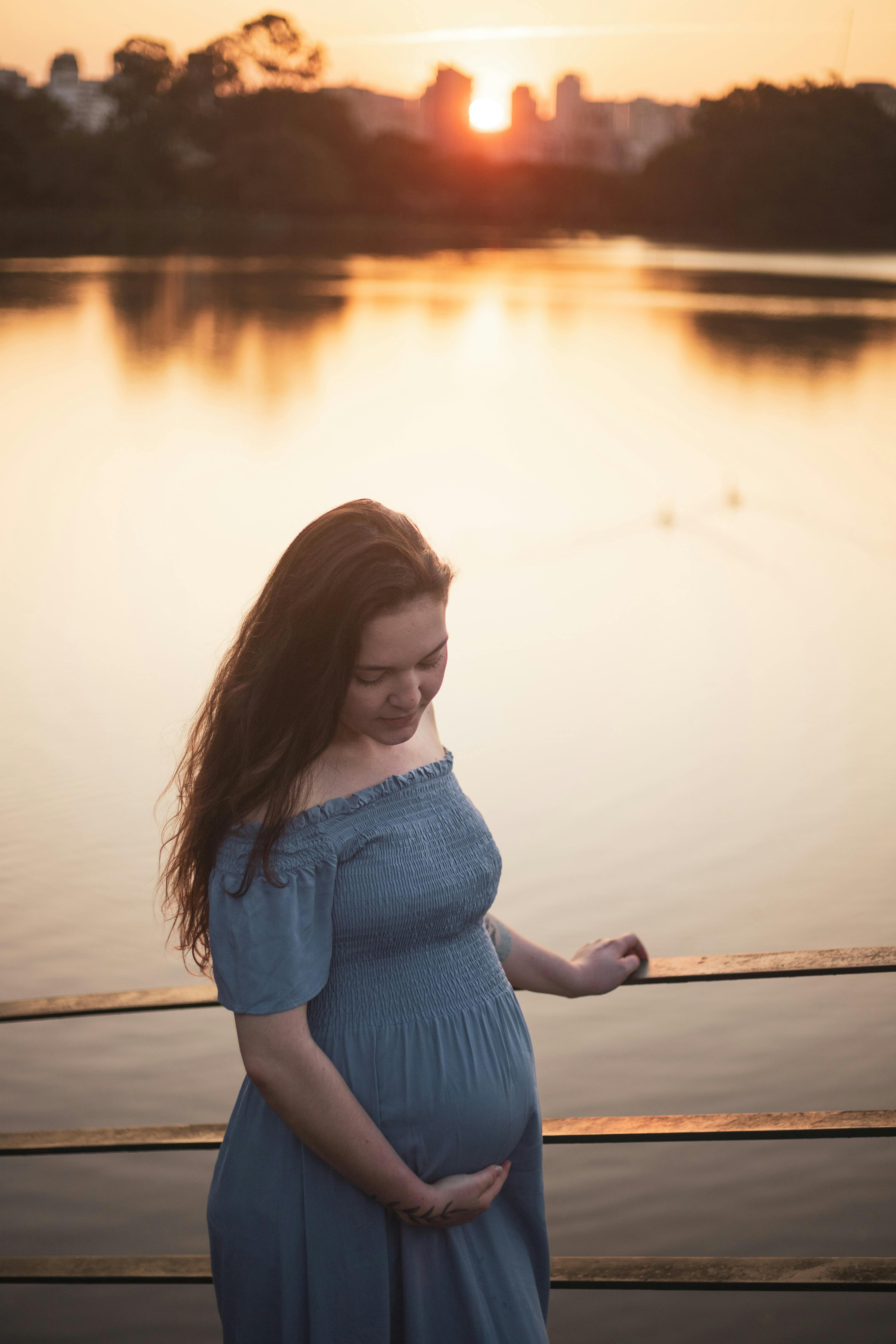 a pregnant woman standing on a dock at sunset