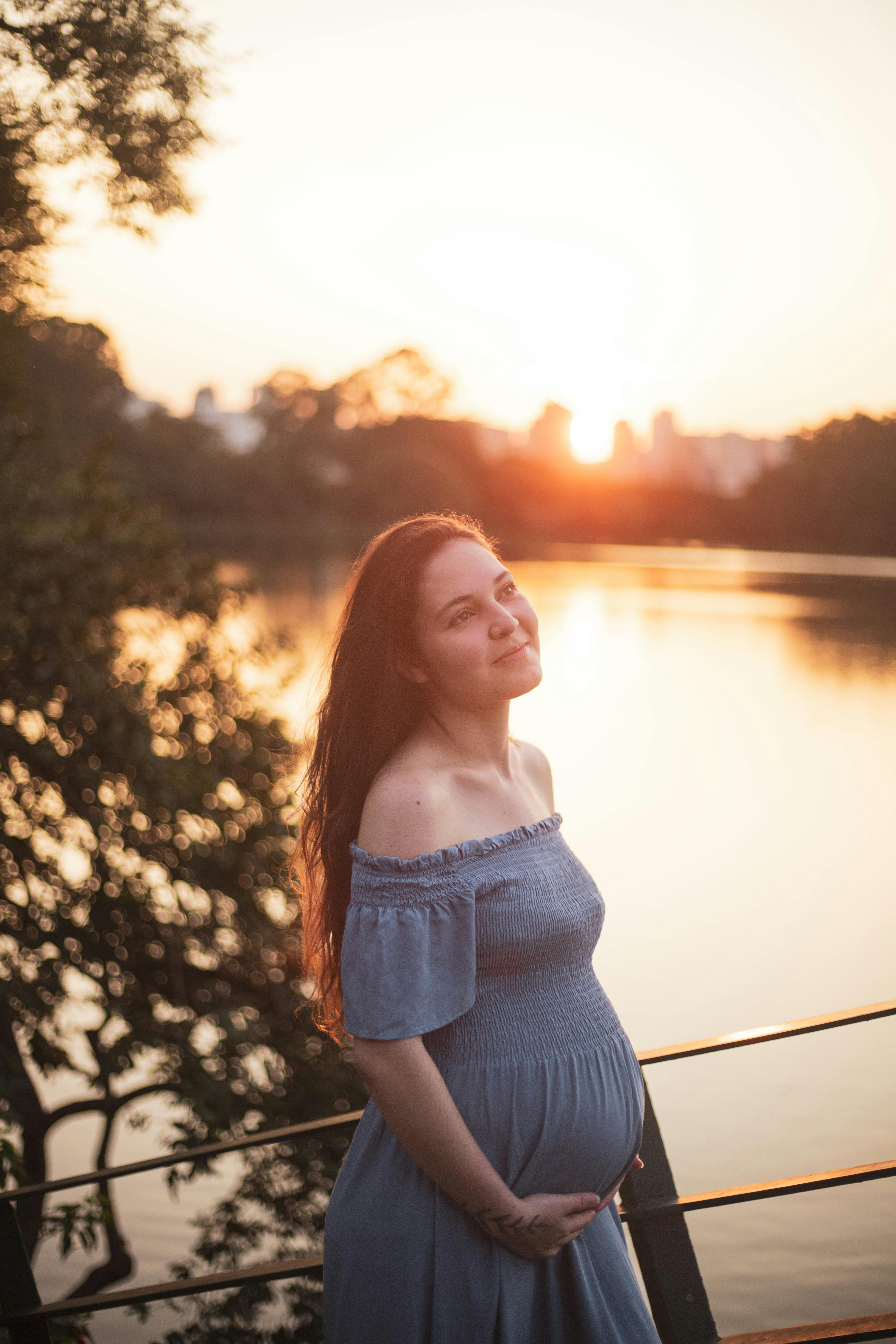 a pregnant woman in a blue dress stands by the water