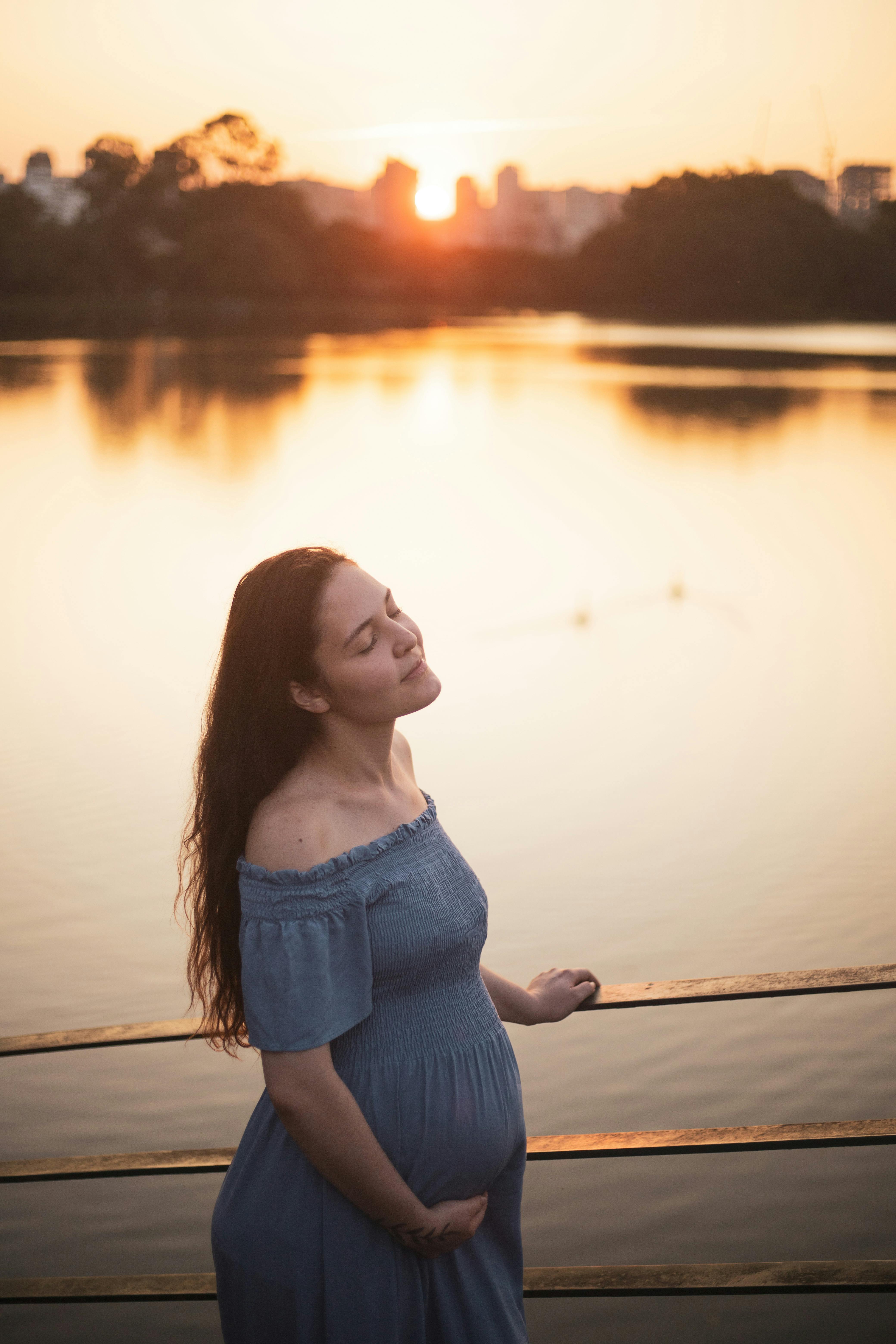 a pregnant woman standing on a pier looking at the sunset