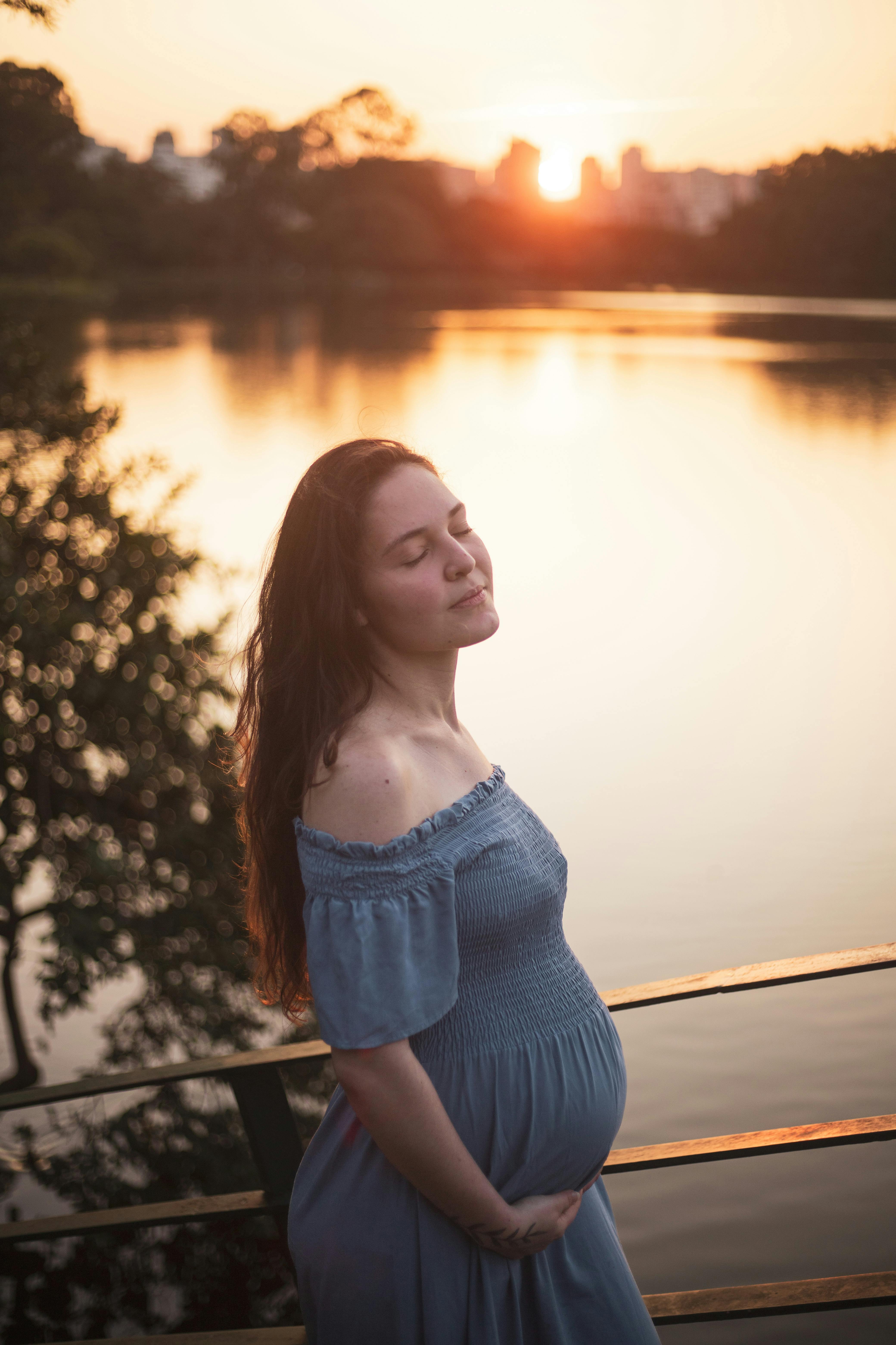 a pregnant woman in a blue dress stands by the water