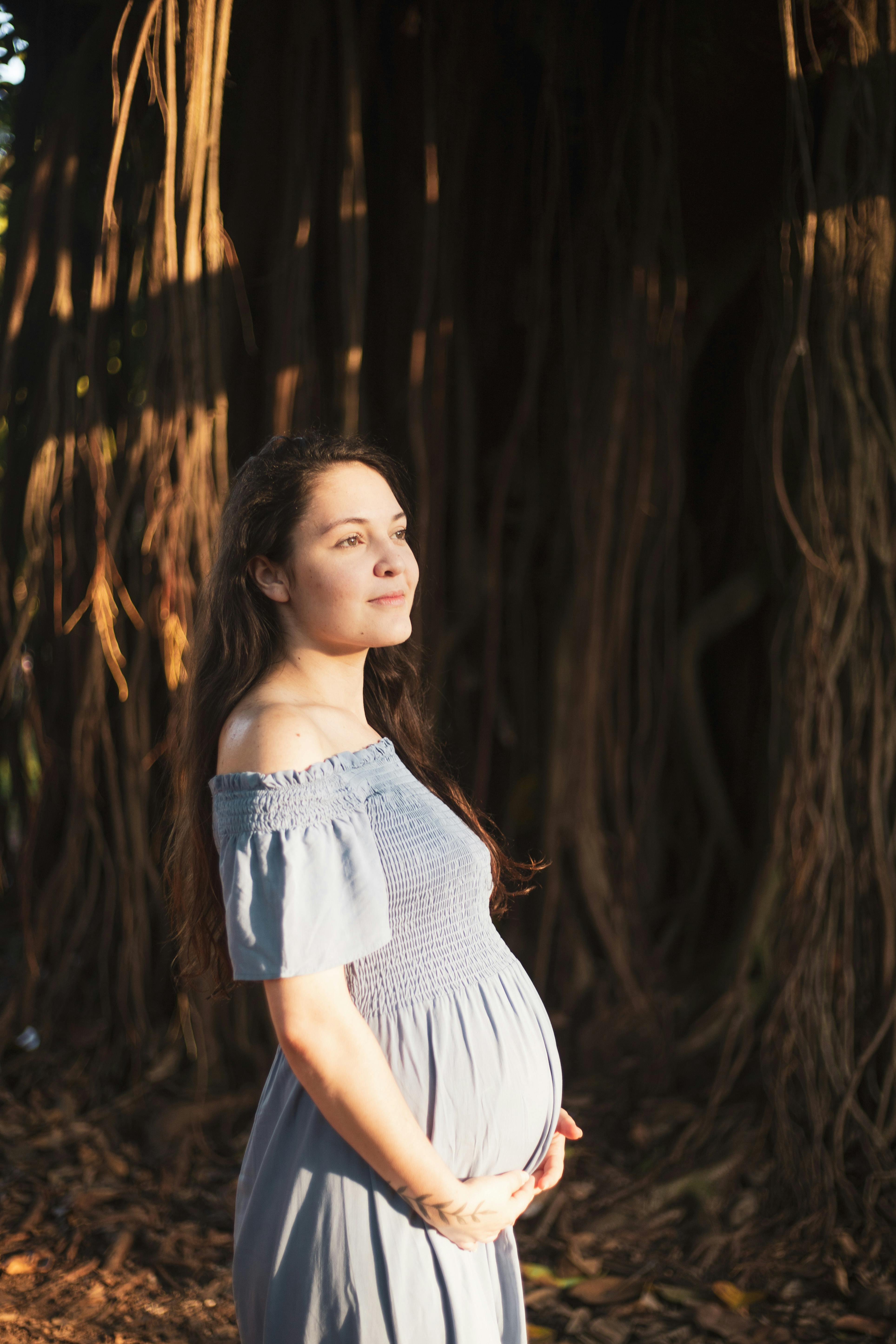 a pregnant woman standing in front of a tree