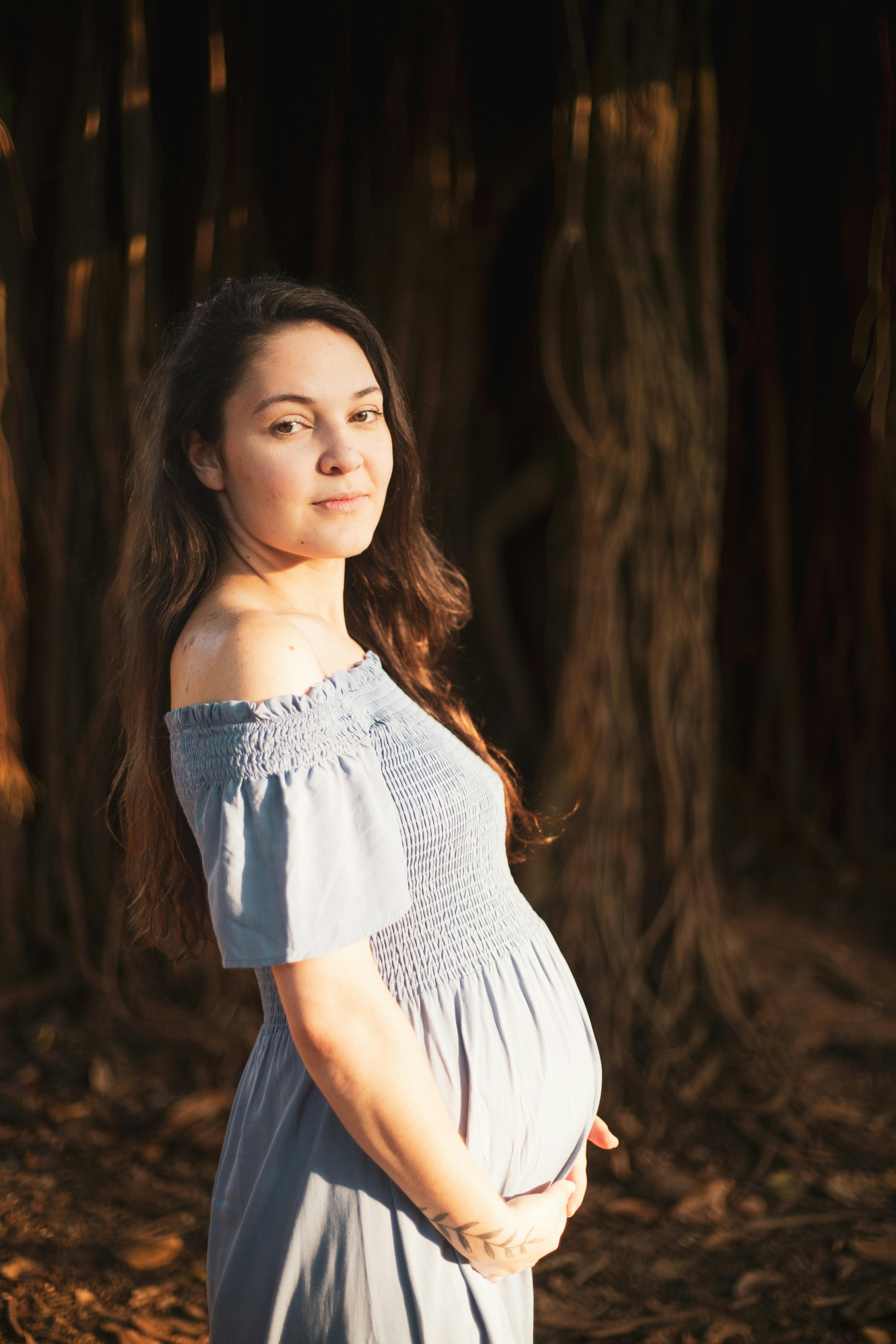 a pregnant woman in a blue dress stands in the woods