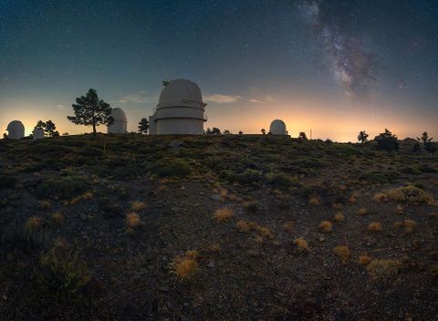 Observatory domes on a scrubby hilltop with the Milky Way rising behind them
