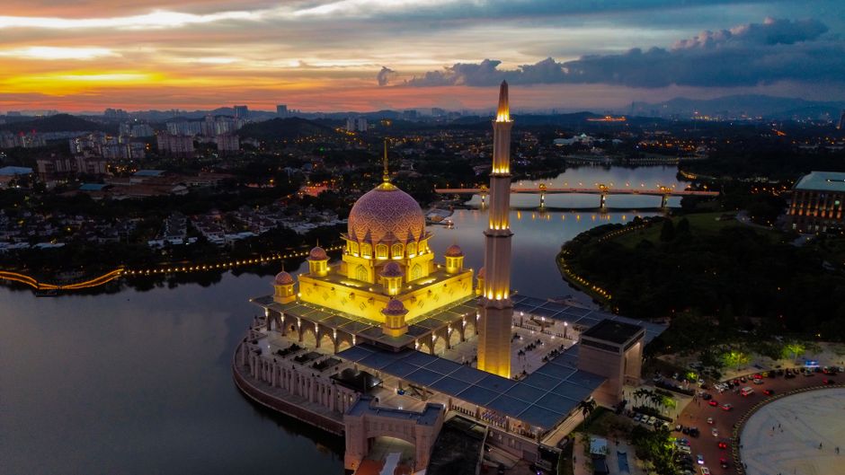 Aerial photograph of the illuminated Putra Mosque with a breathtaking sunset backdrop in Putrajaya, Malaysia.