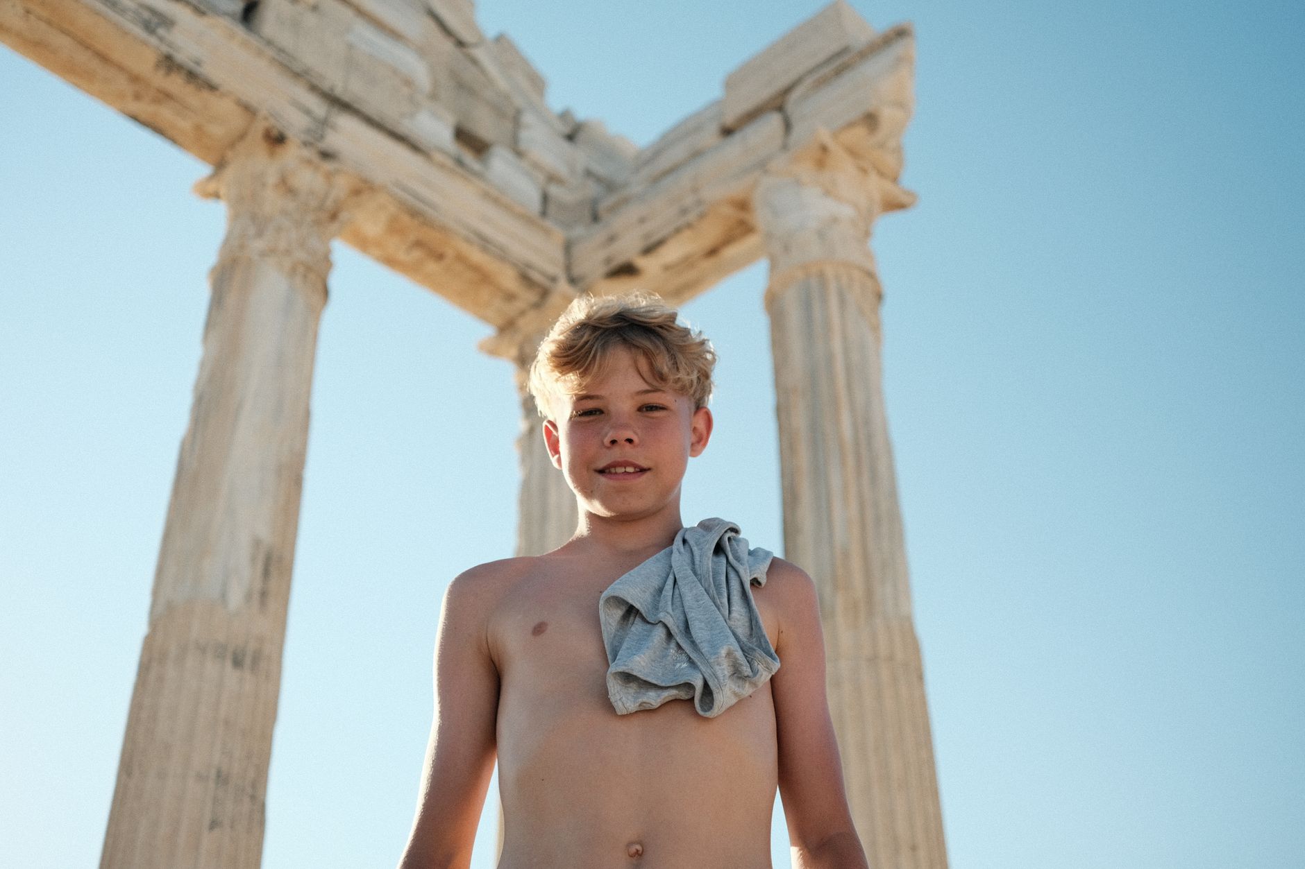 Smiling boy stands confidently before ancient temple ruins under a clear blue sky.
