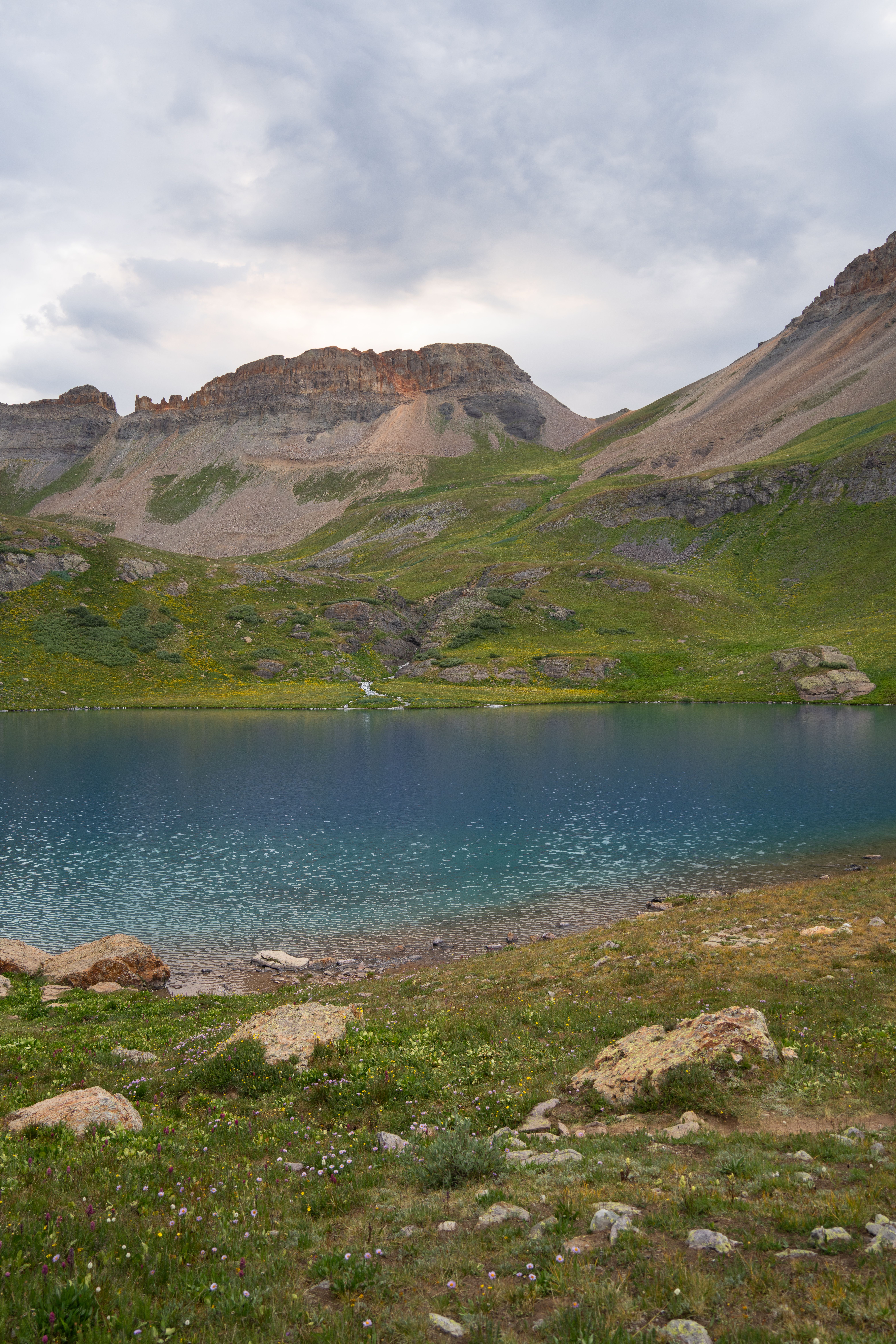 A mountain lake surrounded by grass and rocks · Free Stock Photo