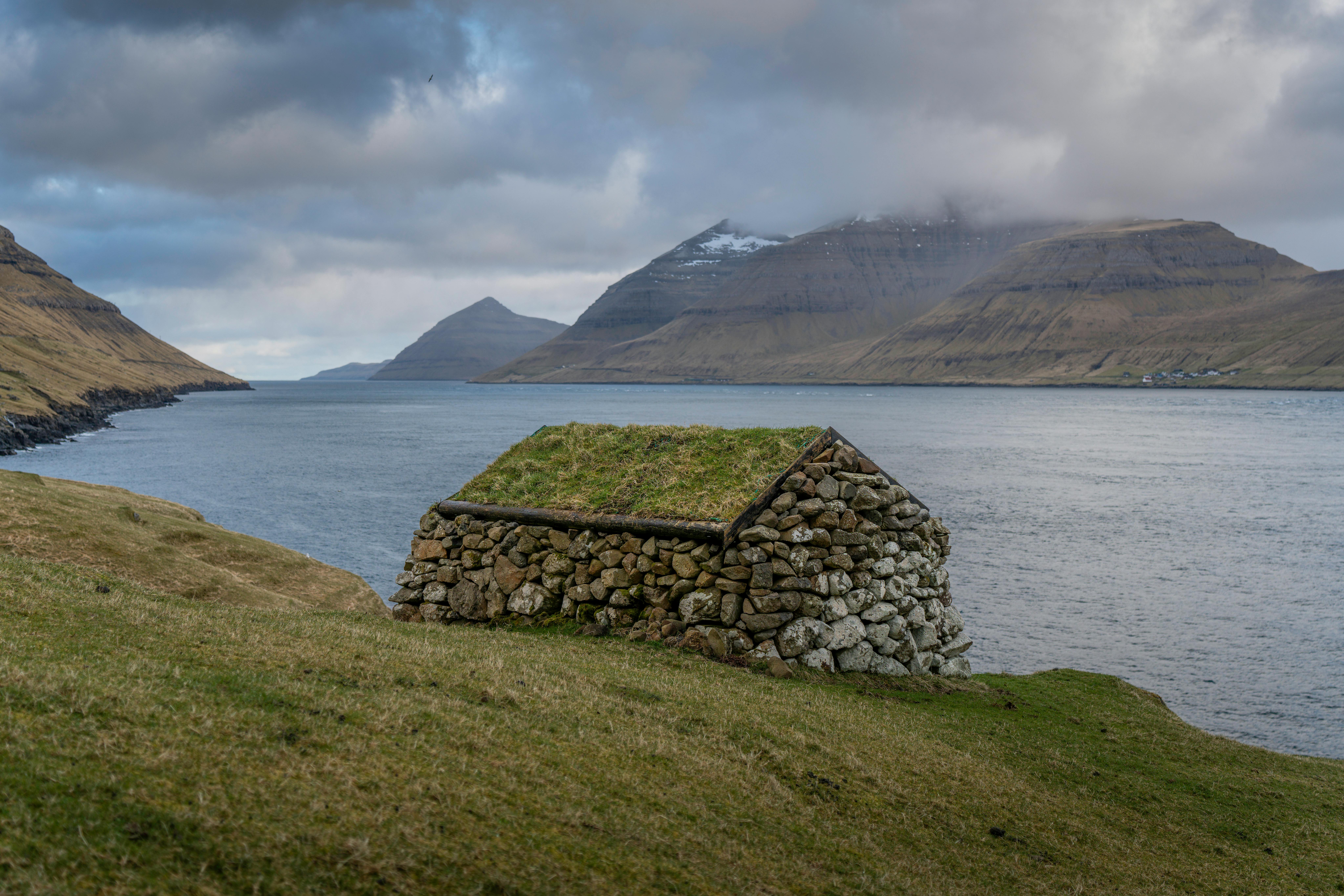 Rustic stone hut with grass roof overlooking the coastal mountains of the Faroe Islands.