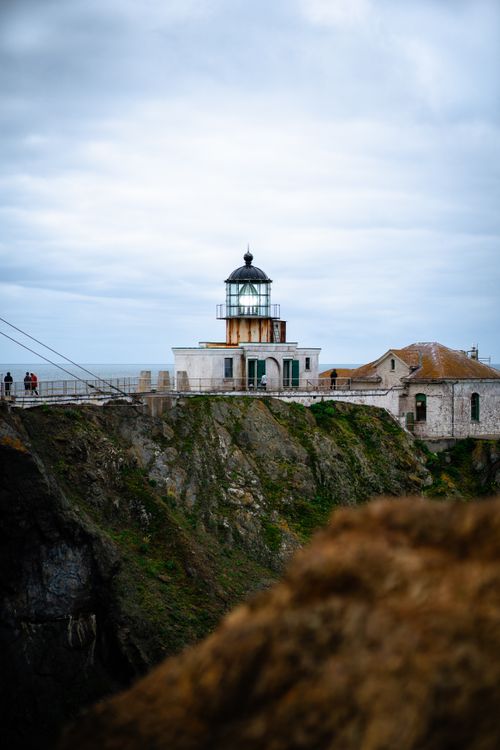 Free A picturesque lighthouse perched on a rugged coastal cliff under cloudy skies. Stock Photo