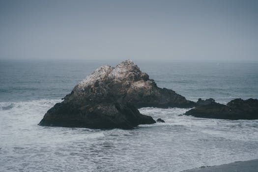 Serene view of rugged rocks amidst ocean waves on a cloudy day.