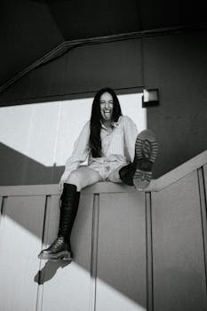 Black and White Shot of a Young Woman Sitting on a Railing and Sticking her Tongue Out 