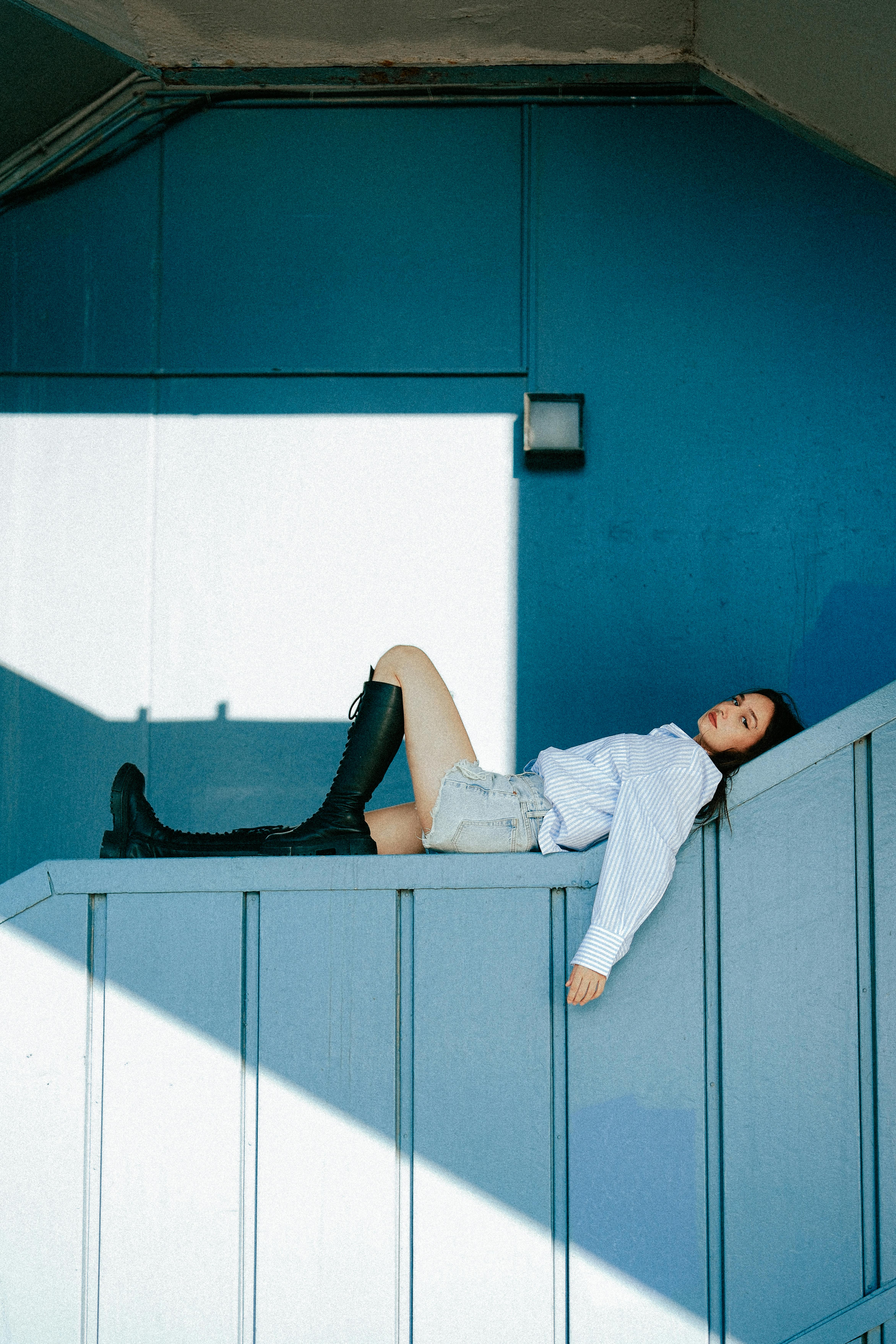 Woman reclining on a blue staircase in stylish outfit with boots, capturing a modern aesthetic.