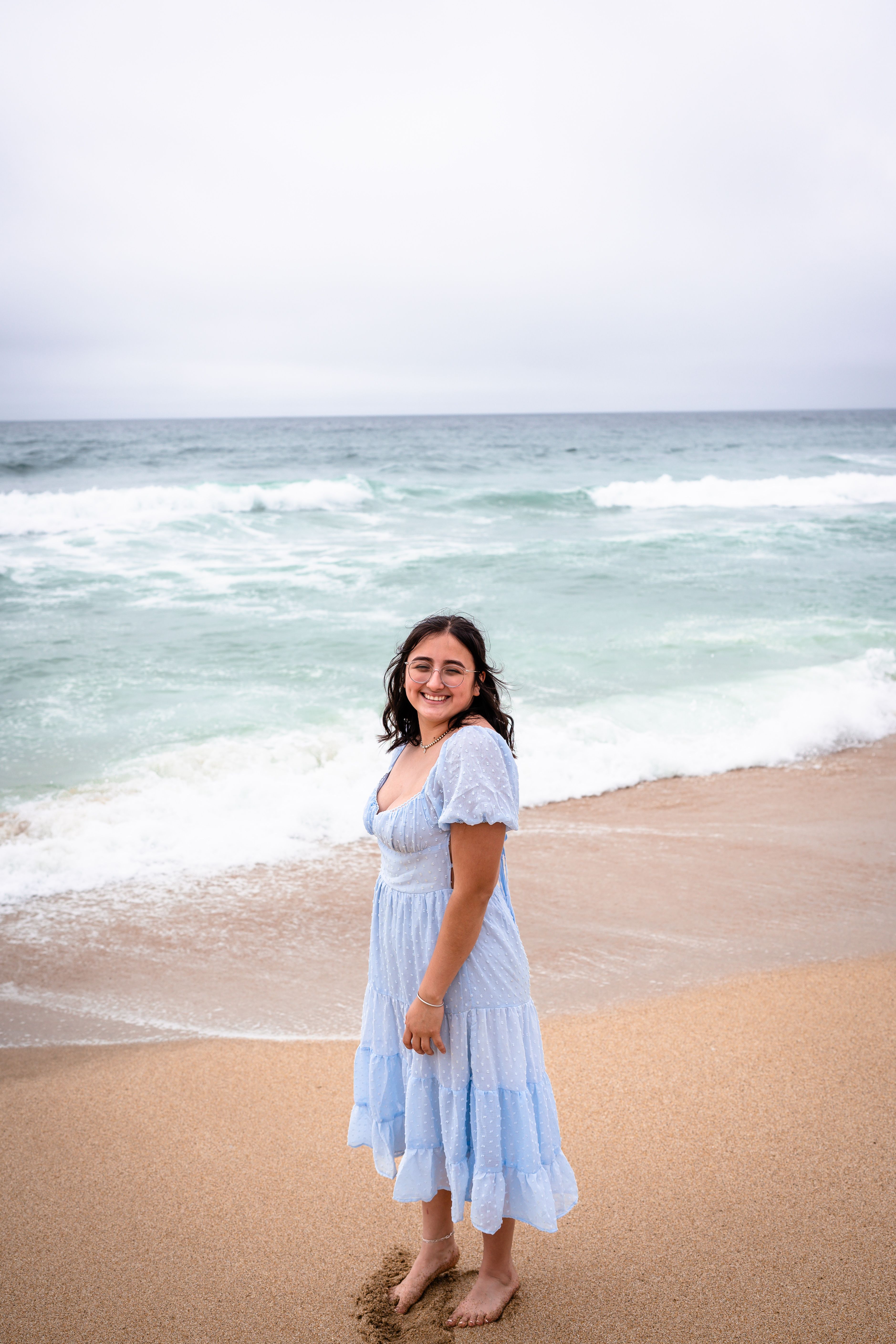A young woman in a blue dress stands on the beach · Free Stock Photo
