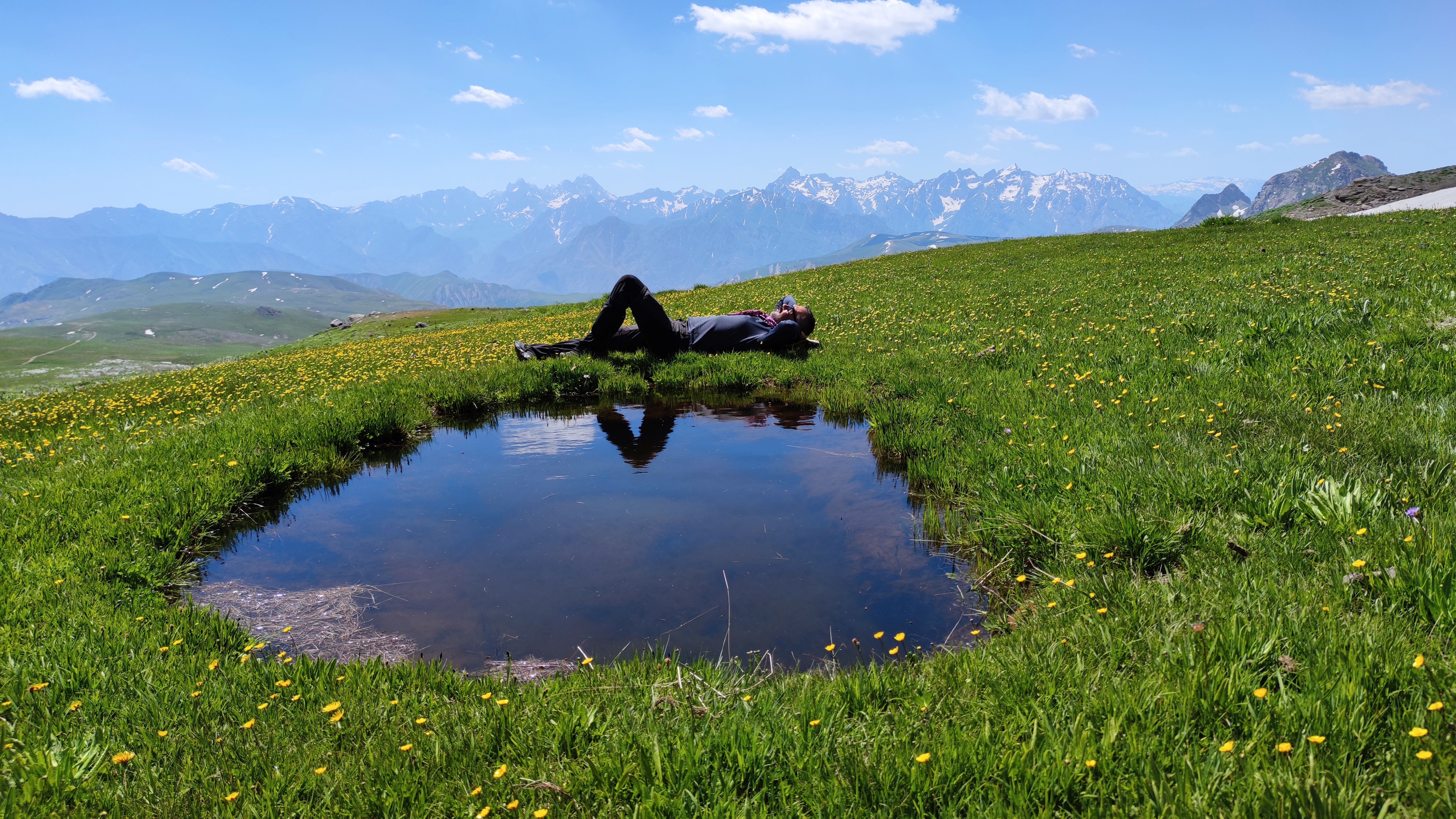A person laying on the grass next to a small pond · Free Stock Photo