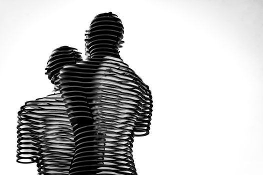 Minimalist black and white abstract sculpture of human figures with a swirling design against white background.