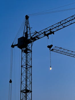 Silhouette of a tower crane standing tall against a blue twilight sky.