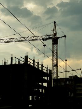 Silhouette of a crane and building under construction during sunset in an urban setting.