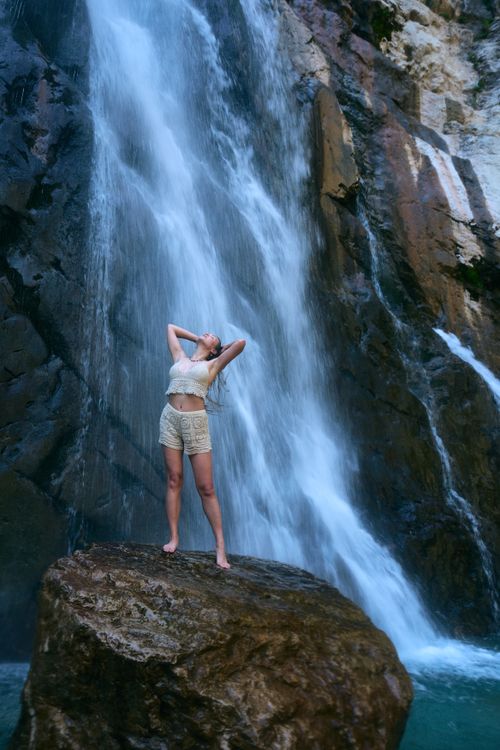 Free Woman standing on a rock under a waterfall in Abkhazia, embracing nature's beauty. Stock Photo