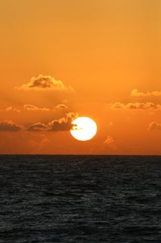 A serene sunset over the ocean with vibrant orange hues and scattered clouds.