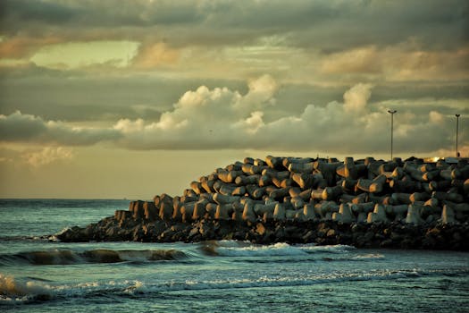 Concrete breakwater at sunset with ocean waves and dramatic sky.