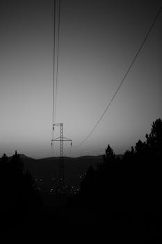 Dramatic silhouette of power lines against a twilight sky with distant mountains.