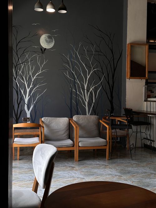 Free Stylish indoor seating area featuring a moonlit wall mural with bare trees and contemporary furniture. Stock Photo