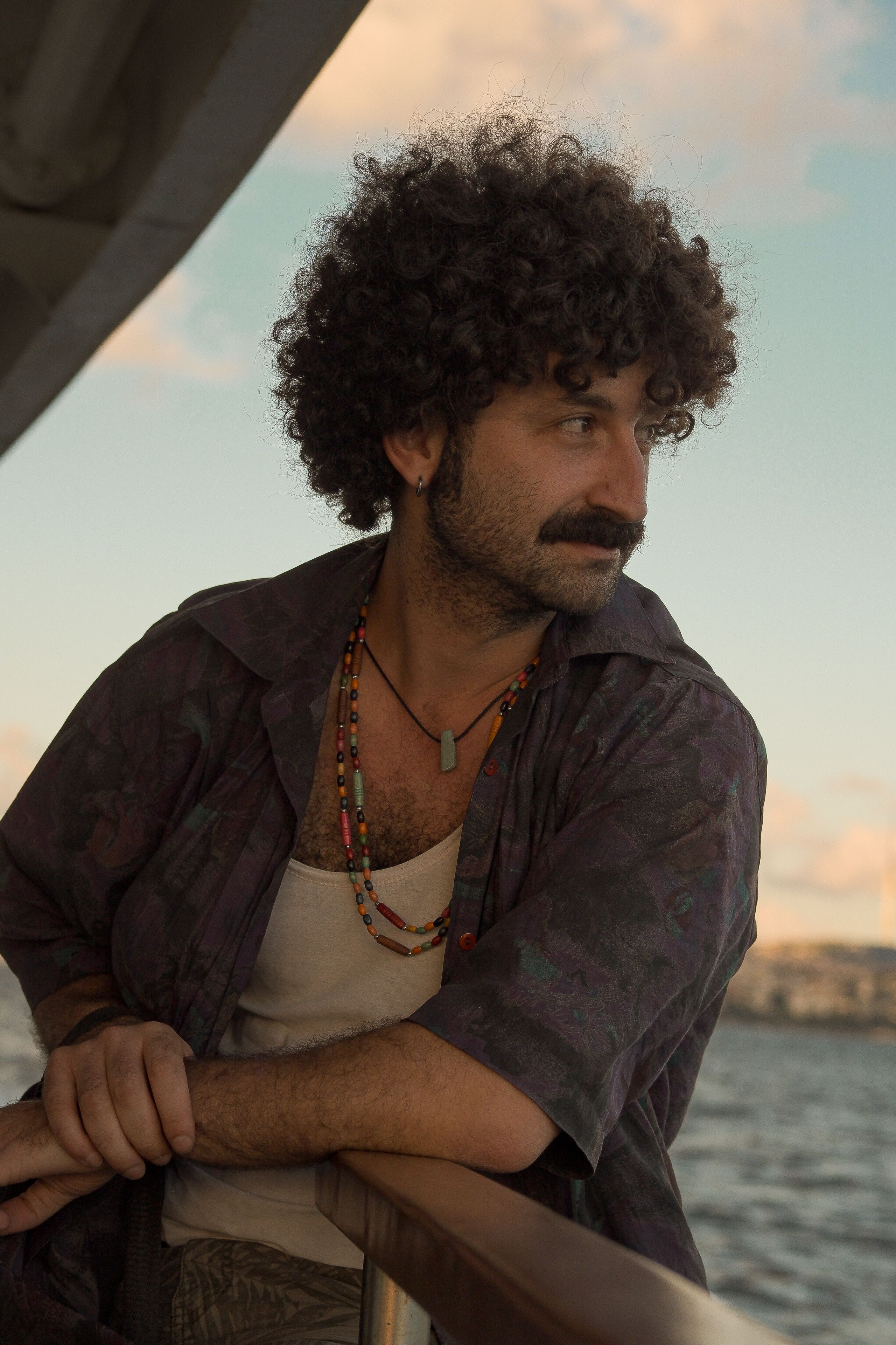 A man with curly hair enjoys a scenic sunset on a boat ride.