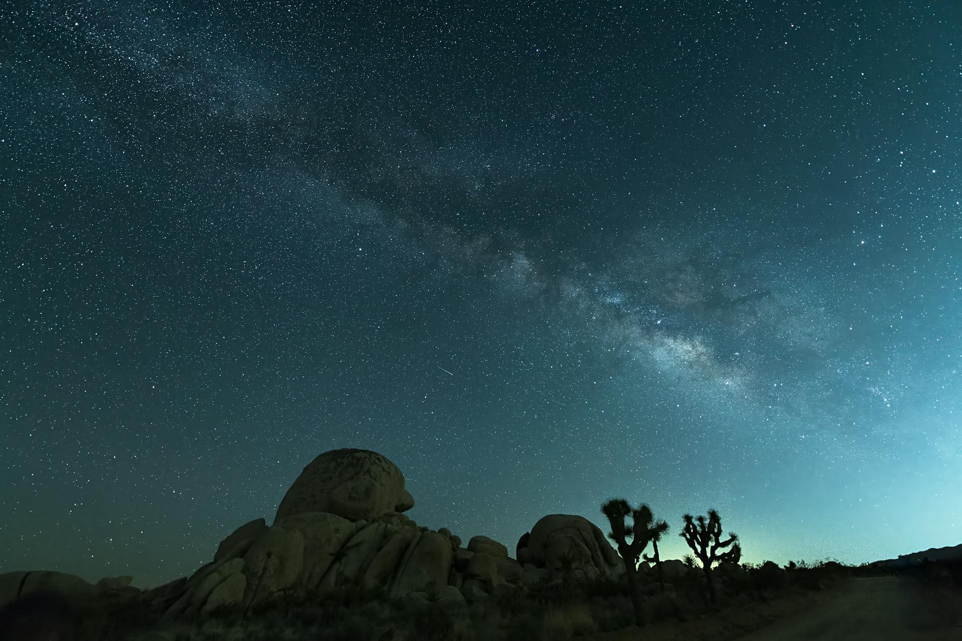 Stunning view of the Milky Way galaxy above desert rocks and Joshua trees under a clear night sky.