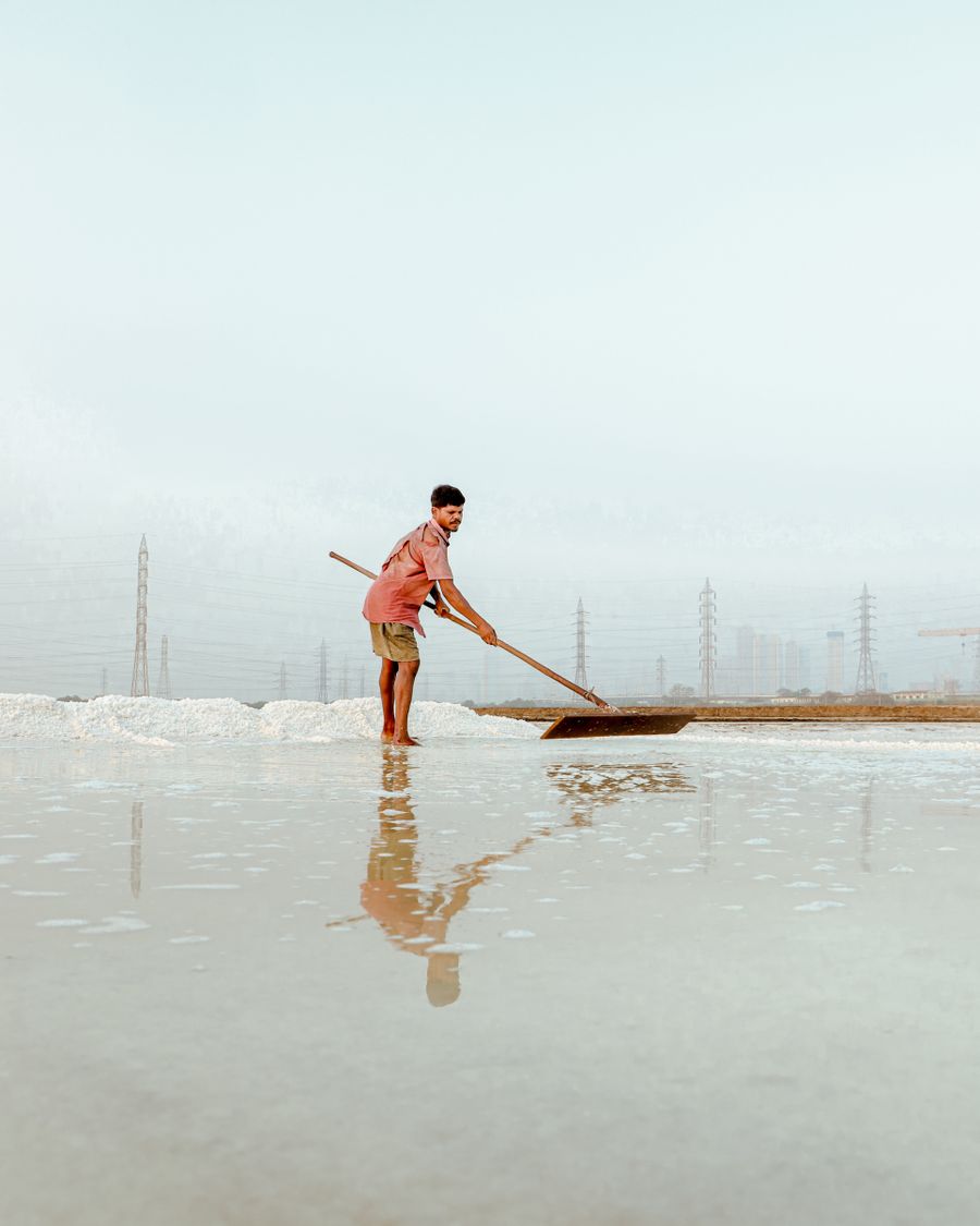 A salt worker raking the shallow water of an evaporation pan