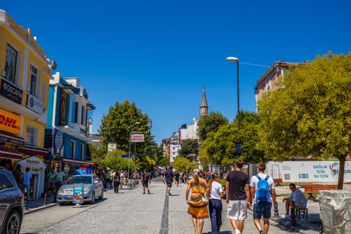 Free Busy urban street with people walking, shops and trees under bright summer sunlight. Stock Photo
