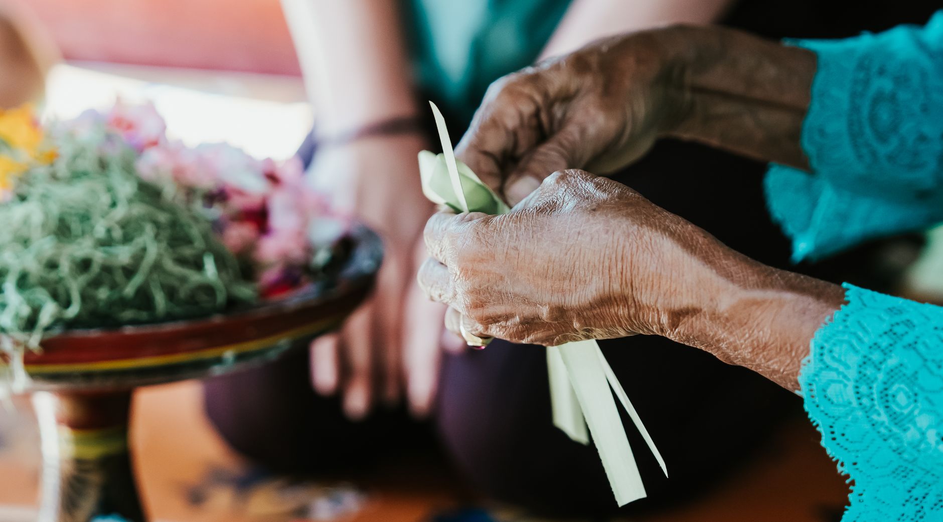 Bàn tay người Bali cẩn thận buộc cựa kim loại cho gà trống trước trận đấu, nền sân làng mờ phía sau