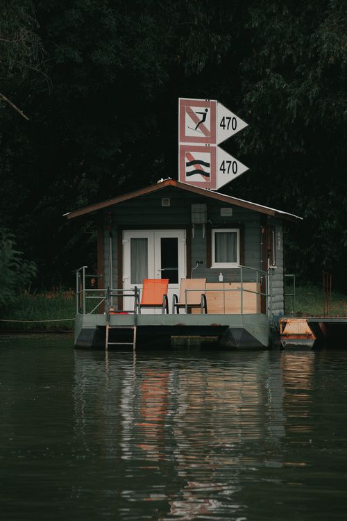 Free A serene houseboat floats on a Hungarian river, reflecting lush greenery. Ideal for travel and nature enthusiasts. Stock Photo
