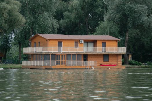 Charming wooden house nestled by a river in Hungary, surrounded by lush greenery.