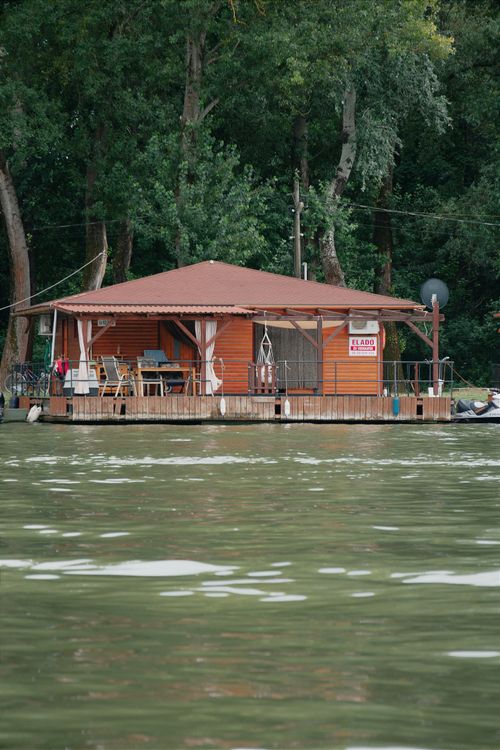 Free Cozy wooden house with a red roof on a peaceful lake, surrounded by lush greenery in Hungary. Stock Photo