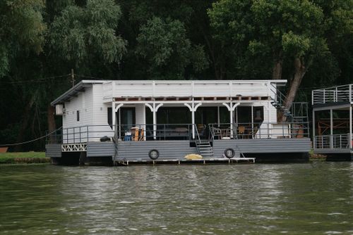 Free A serene houseboat moored along a lush, green riverside in Hungary, perfect for a peaceful retreat. Stock Photo